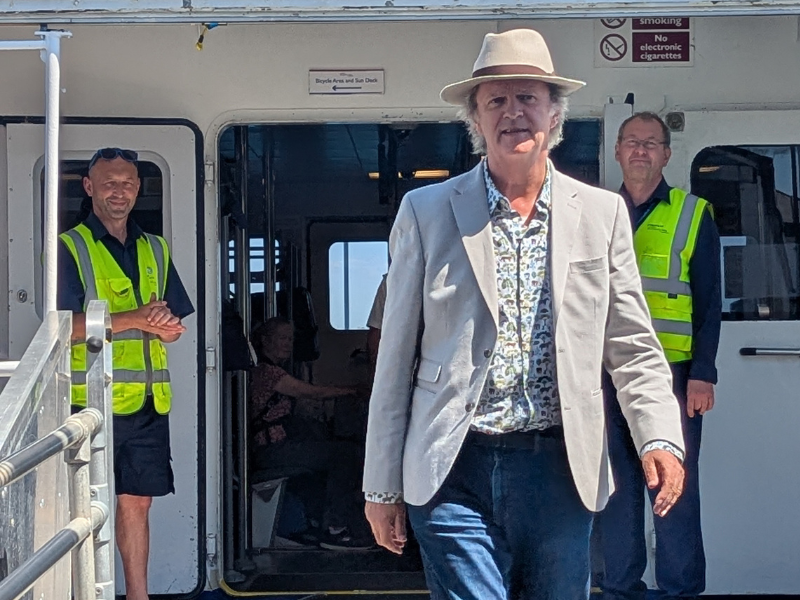 Comedian Paul Merton steps of a Wightlink FastCat, there are two staff members behind him in hi vis uniform