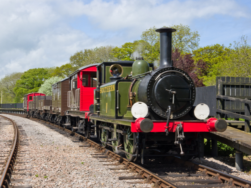 A steam train on the rails on the Isle of Wight. It is red, black and green in colour.
