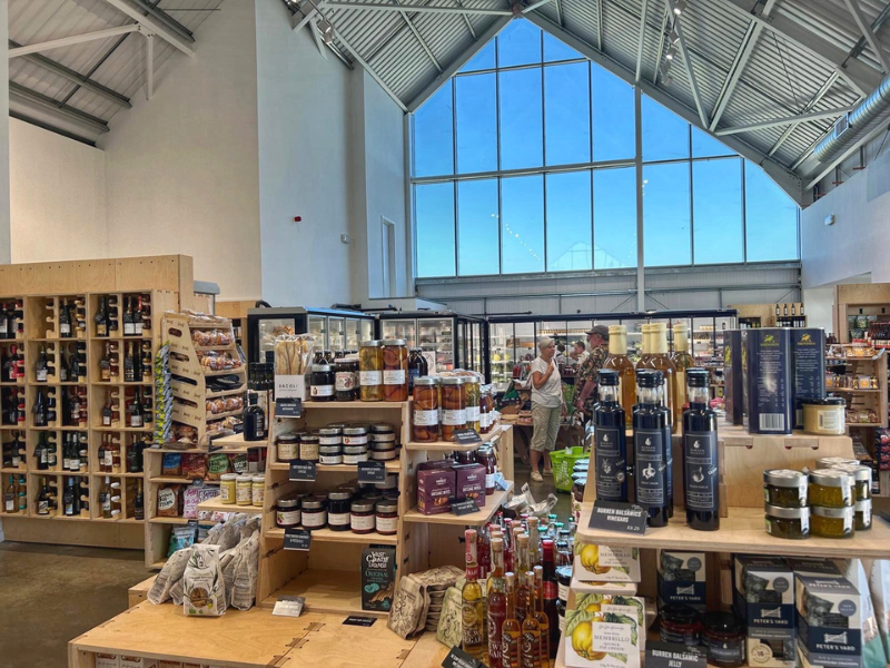 A modern farm shop showing lots of local produce on the shelves and a vaulted glass ceiling