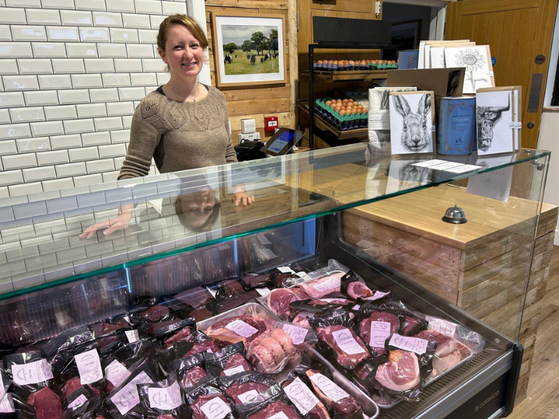 A woman standing behind a meat counter at a modern-looking farm shop.