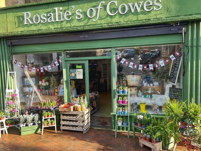 A quaint green-painted shop with plants outside and bunting in the window, in Cowes on the Isle of Wight