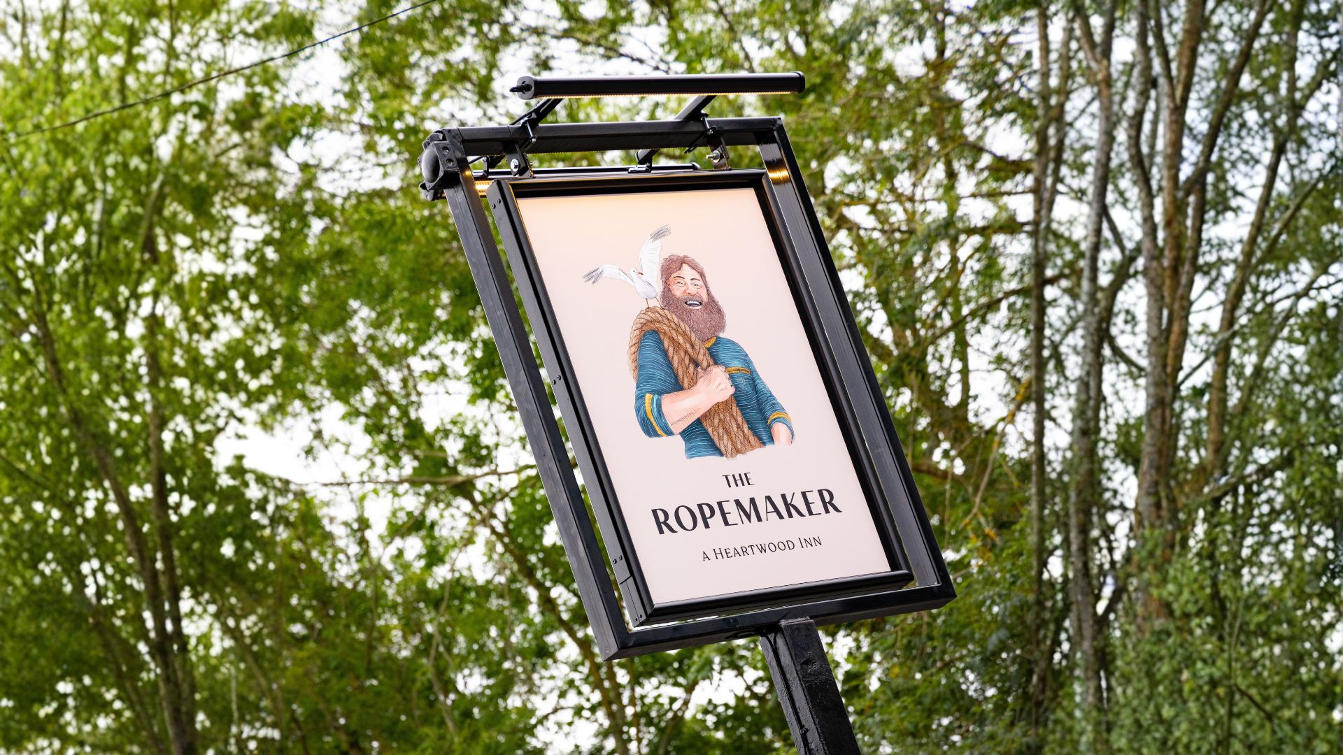 Sign for The Ropemaker pub featuring an illustrated figure with rope, set against trees outdoors.