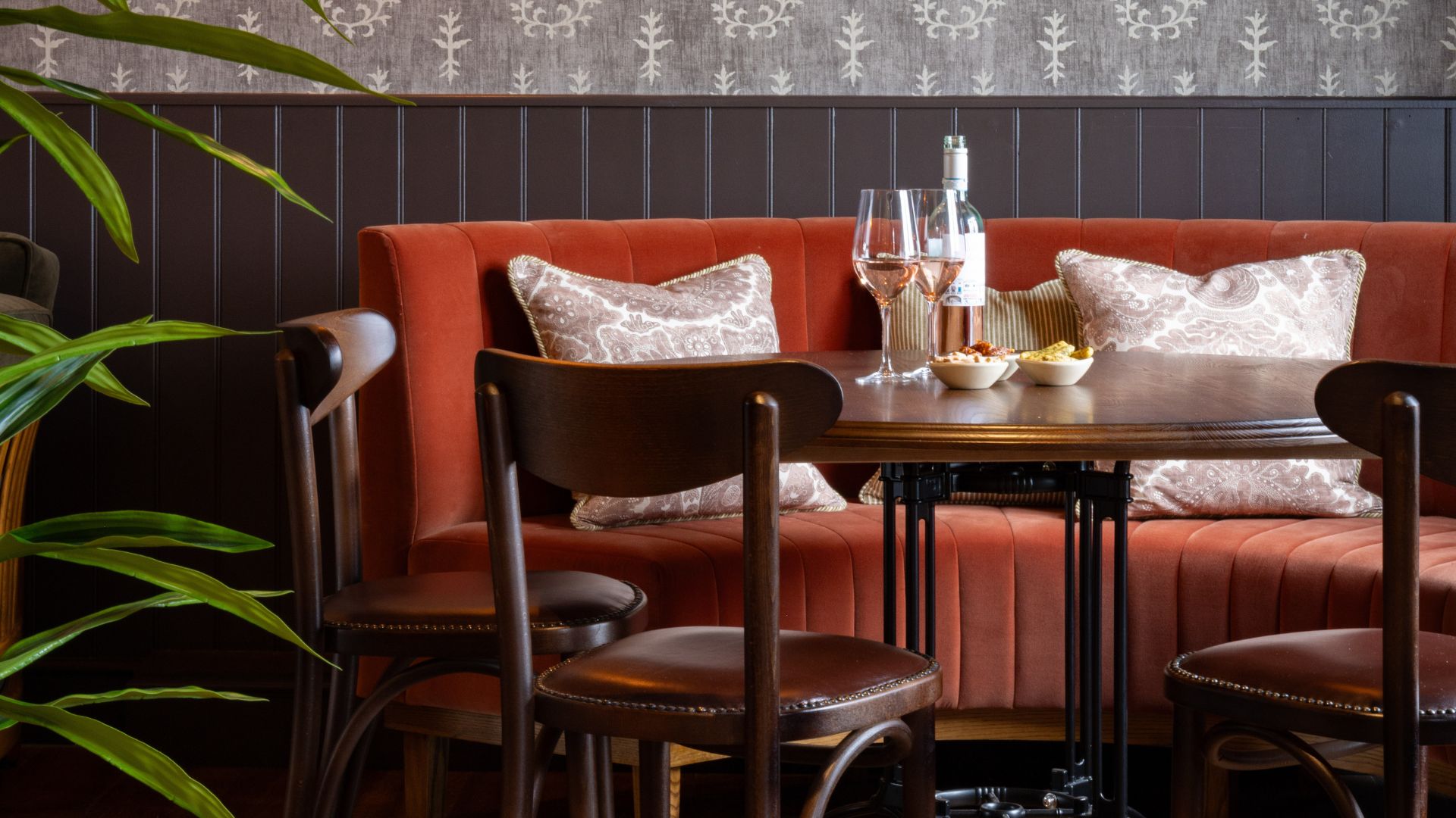 Cosy restaurant booth at The Ropemaker with a table set for drinks and snacks, featuring wine glasses, cushions and warm interior décor.
