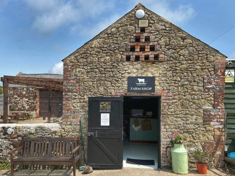 A traditional farm outbuilding with the door open. It's made of stone and there is a farm shop inside