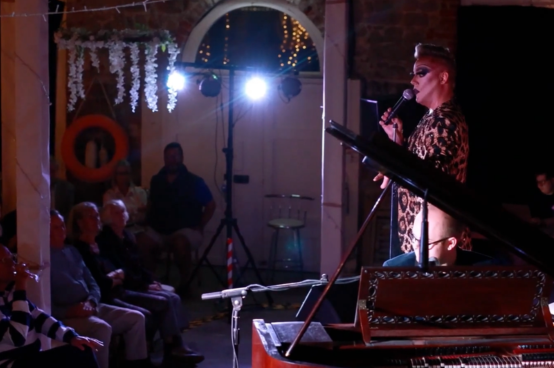 Singer performing on stage at Cowes Fringe with audience watching in a small indoor venue