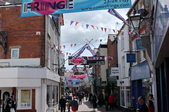 Crowds walking through Cowes high street decorated with Cowes Fringe banners and bunting