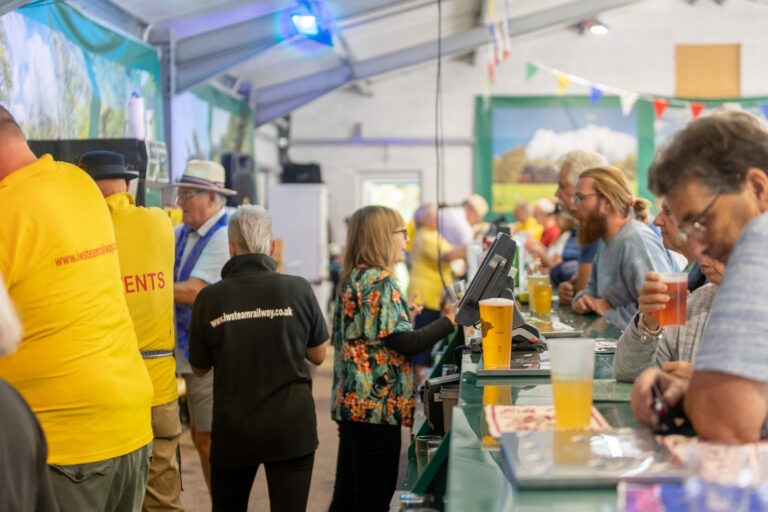 People queuing at a busy indoor bar, being served drinks at a cider festival