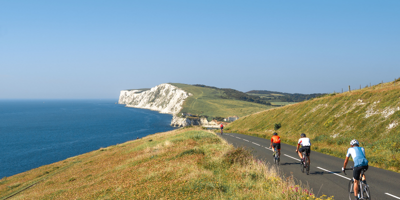 A group of cyclists on a scenic tarmac road on the Isle of Wight, overlooking the coastline