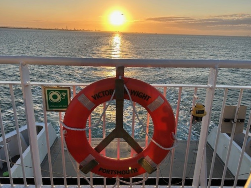 The view of a stern of a ferry taken from a passenger deck at sunrise - there's a life ring in the foreground with 'Victoria of Wight' written on it