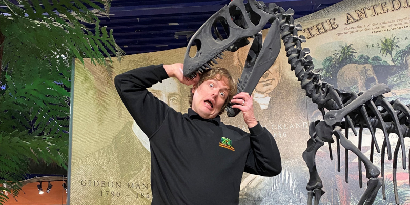 A man with his head in the jaws of a dinosaur skeleton exhibit at Dinosaur Isle Museum on the Isle of Wight