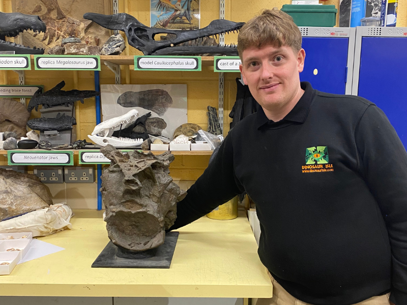 A man inside a museum stands with a dinosaur fossil
