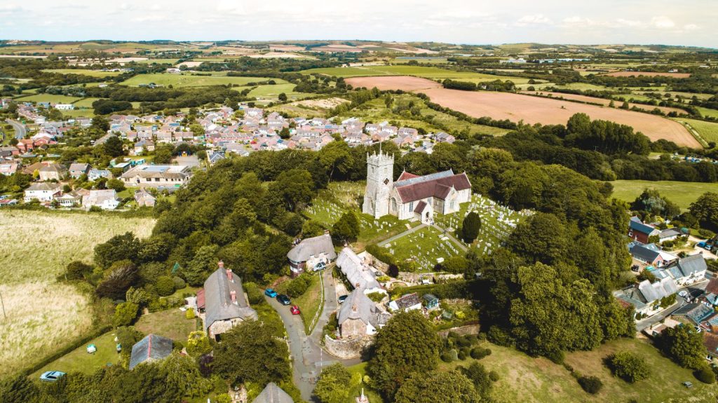 Drone view of Godshill village centred on the historic church, surrounded by thatched cottages, trees and rolling Isle of Wight countryside.