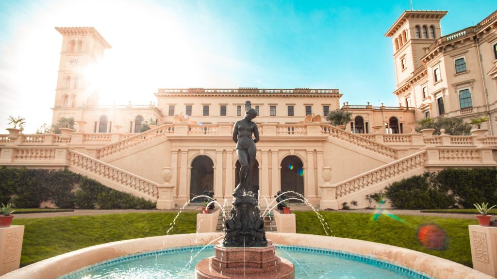 The grand Italianate façade of Osborne House rises behind an ornate fountain and formal terraces, bathed in bright sunshine.