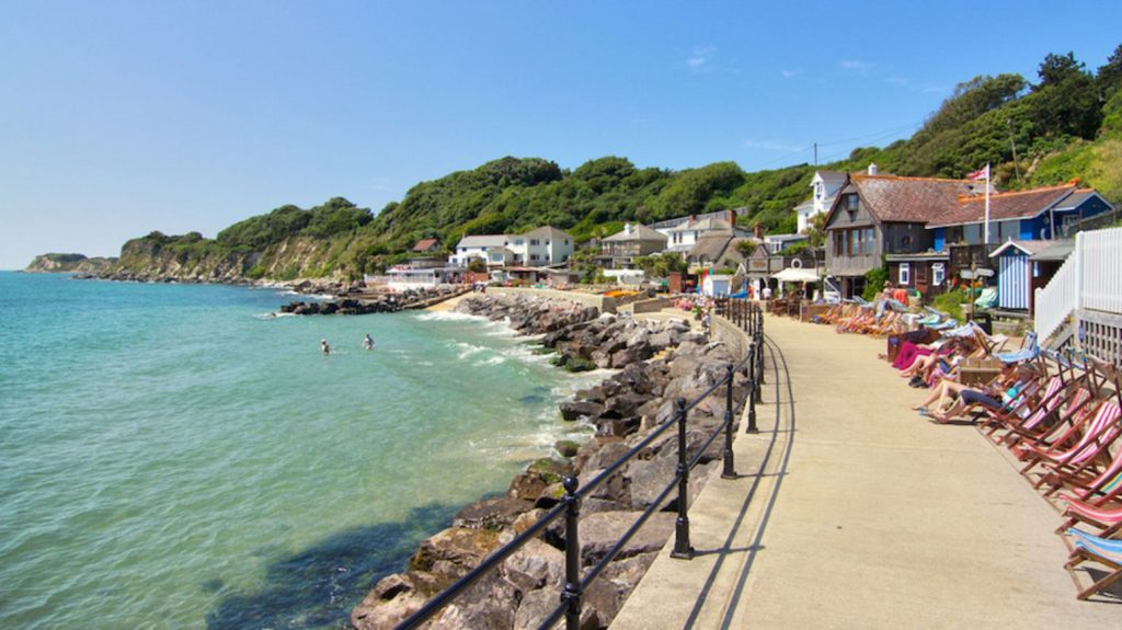 Steephill Cove's waterfront lined with colourful deckchairs, cafés and cottages beside clear turquoise water on a sunny day.