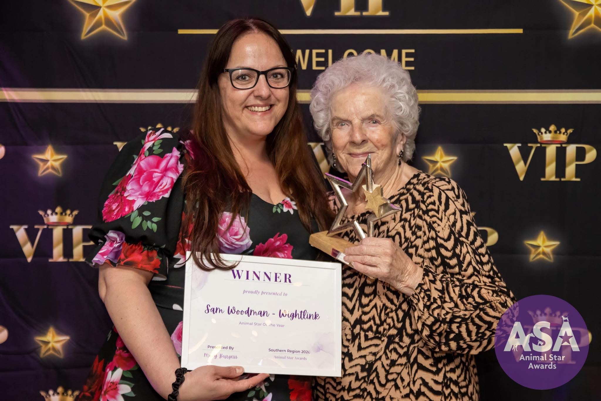 Two people pose with a “Winner” certificate and star trophy at a black and gold Animal Star Awards backdrop.