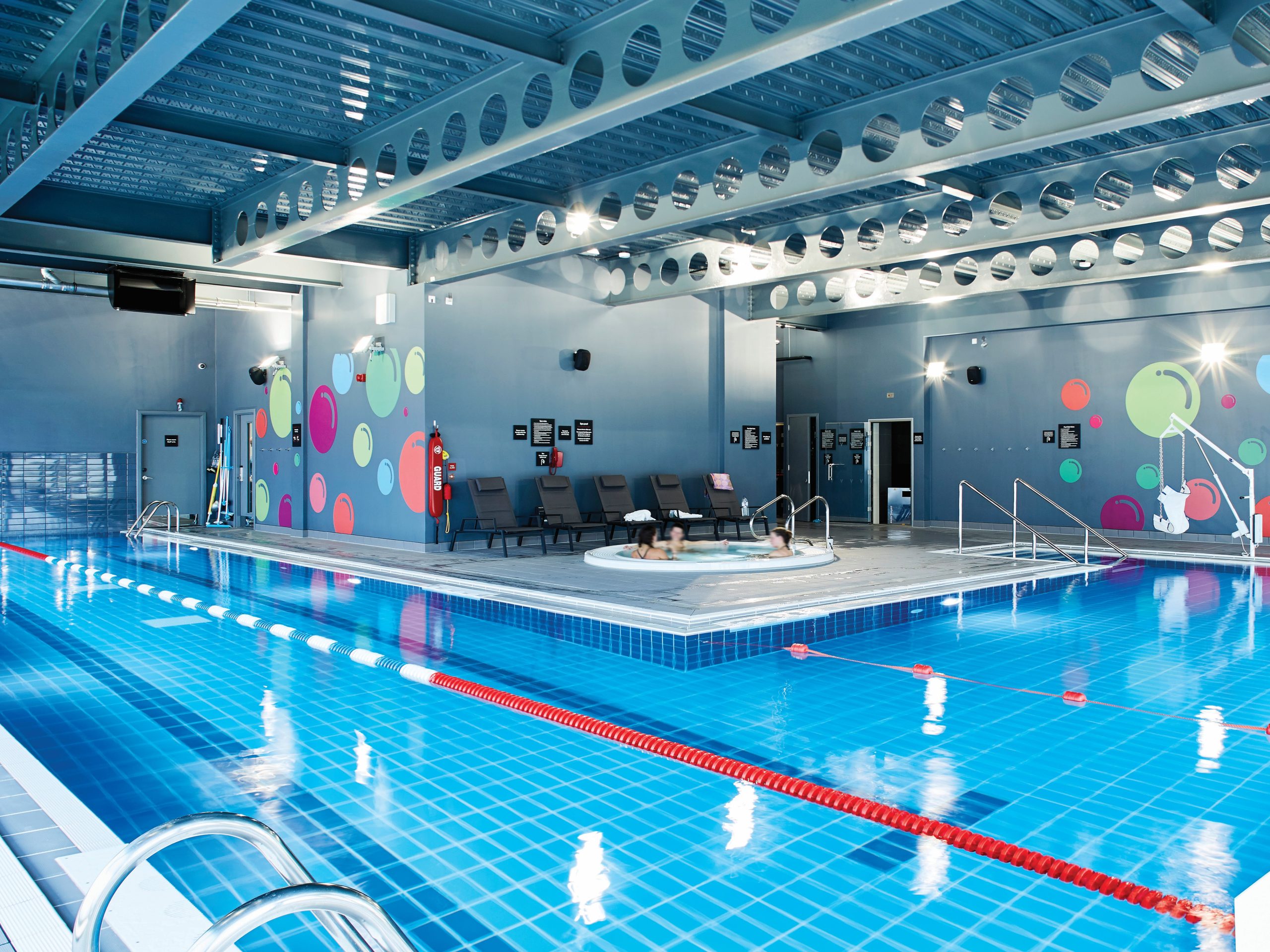 Indoor swimming pool at Village Hotel with lap lanes, jacuzzi area and colourful wall design
