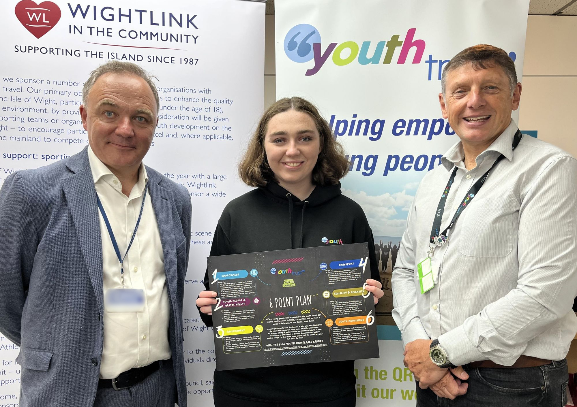 Representatives from Wightlink and the Isle of Wight Youth Trust stand with a young person holding a youth initiative poster, in front of display banners promoting community support.