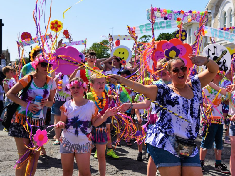 A colourful procession of people waving banners and bright flags as part of a carnival procession