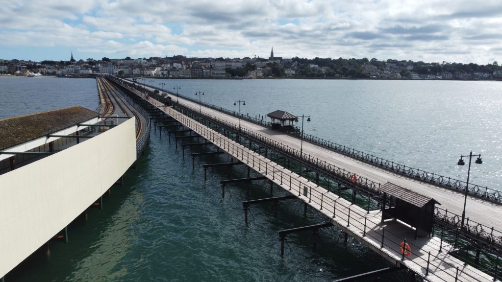 A view along Ryde Pier showing the railway tracks and pedestrian walkway stretching out over the Solent towards Ryde, with the town skyline in the background.