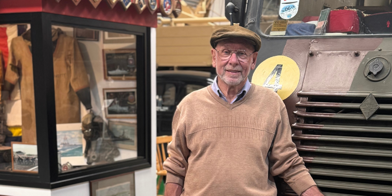 A man wearing a flat cap is standing beside exhibits inside a military heritage museum