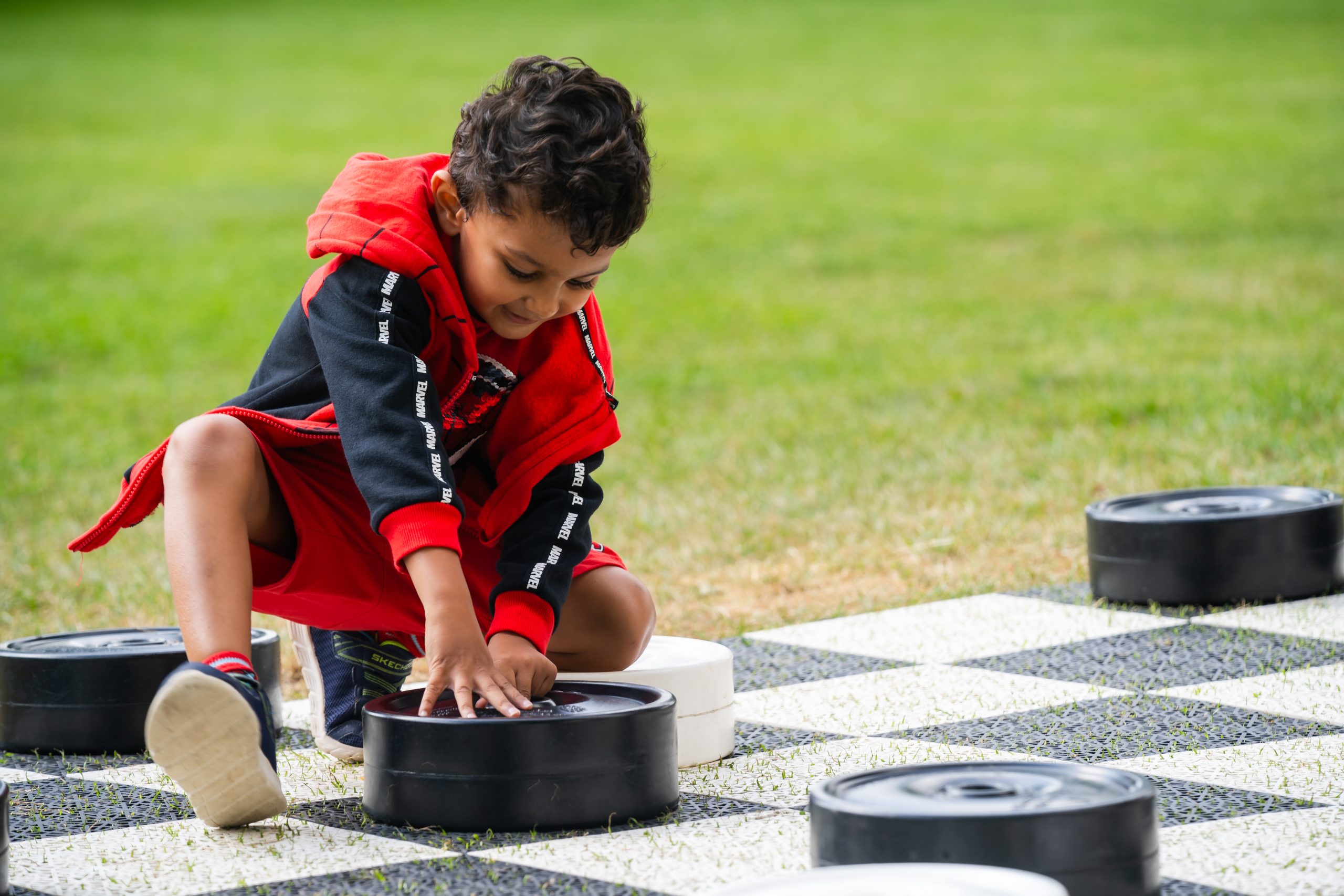 Child playing on a giant outdoor checkers board in the gardens at The Vyne.