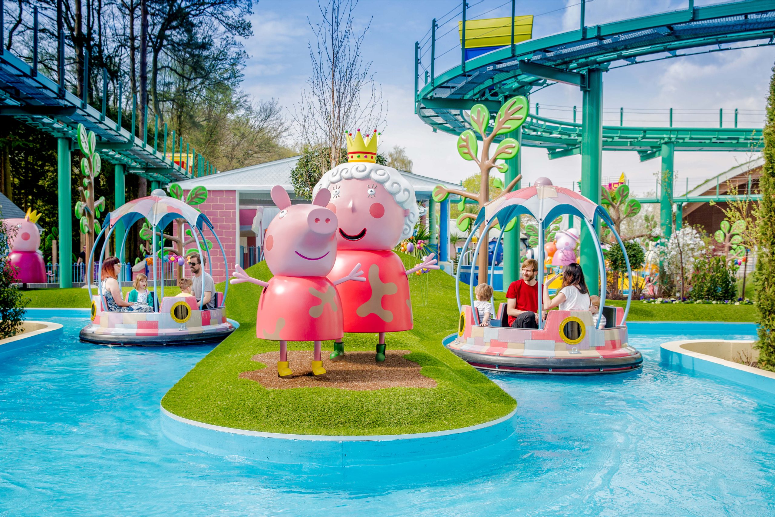The Queen and Peppa Pig figures stand beside the Grampy Rabbit's Sailing Club ride, with guests enjoying boat rides in Peppa Pig World at Paultons Park.