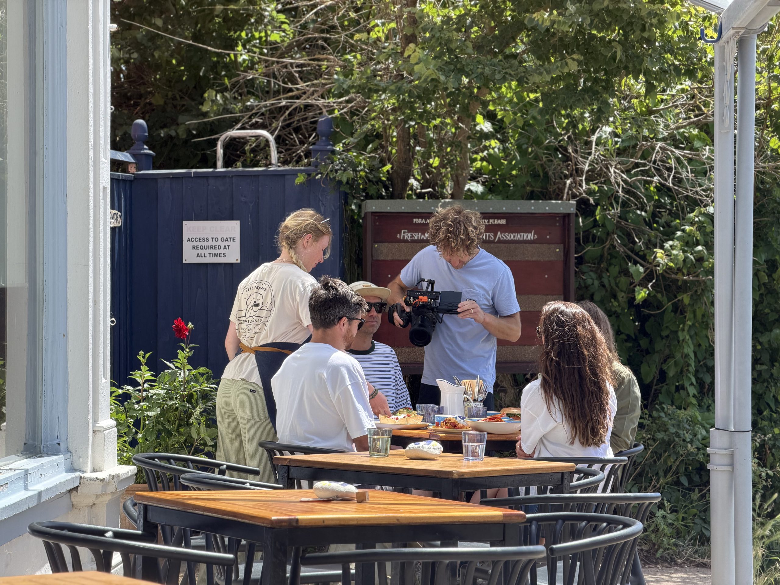 A film crew captures visitors dining outdoors at The Piano Café in Freshwater Bay for Wightlink's 48 Hours on Island Time campaign.
