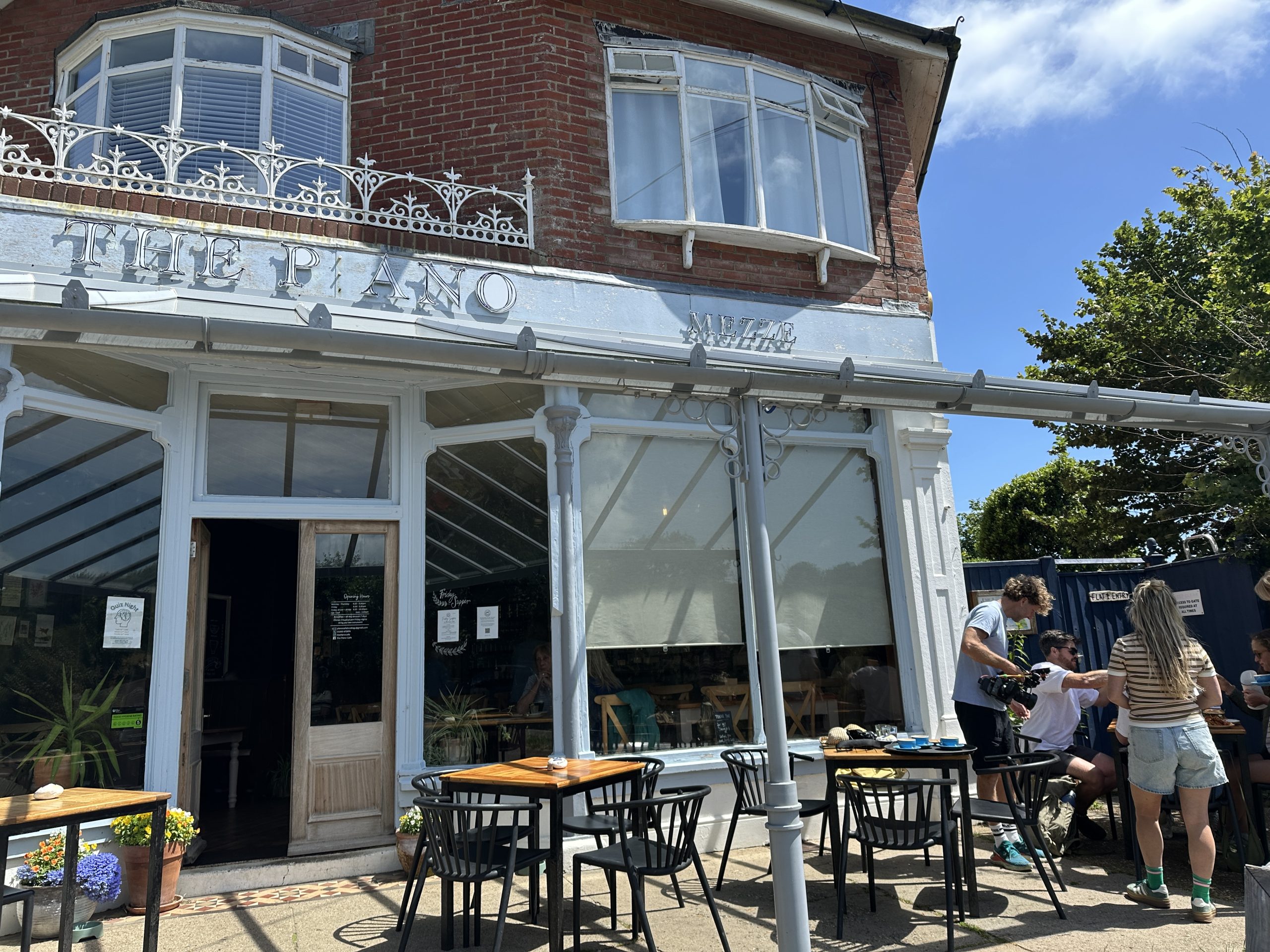 Exterior of The Piano Café in Freshwater Bay with outdoor tables and visitors enjoying the sunny terrace on the Isle of Wight.