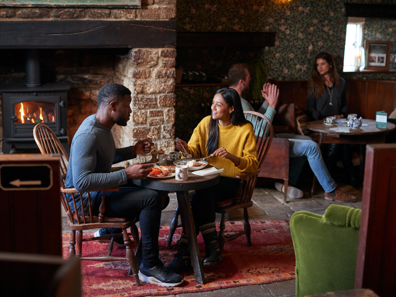 A couple dining at a traditional country pub, with a wood burner in the background