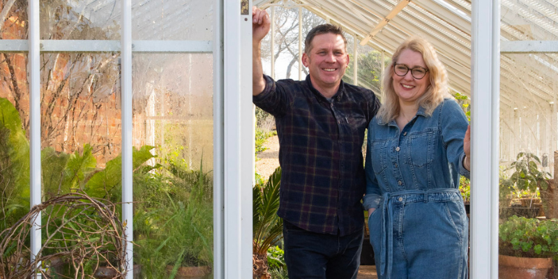 A man and woman, gardeners, stand inside the entrance to a greenhouse at Farringford on the Isle of Wight