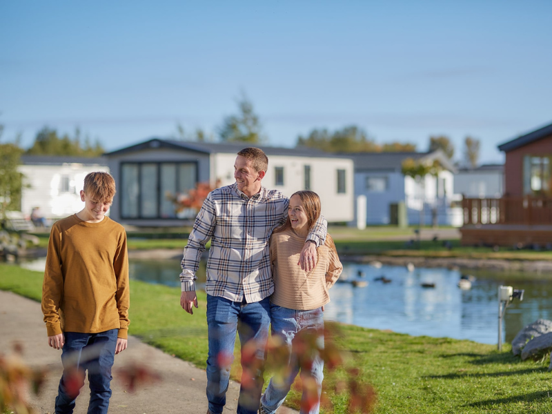 A family walking along the street of a holiday park on the Isle of Wight, with lodges and a lake in the background