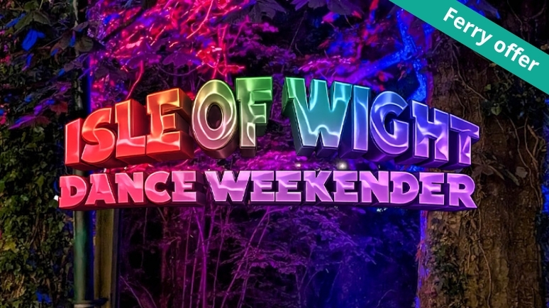 Colourful illuminated sign reading “Isle of Wight Dance Weekender” displayed among trees and woodland foliage at night. Vibrant pink, purple, blue and green lighting creates a festival atmosphere, with a green corner ribbon reading “Ferry offer”.