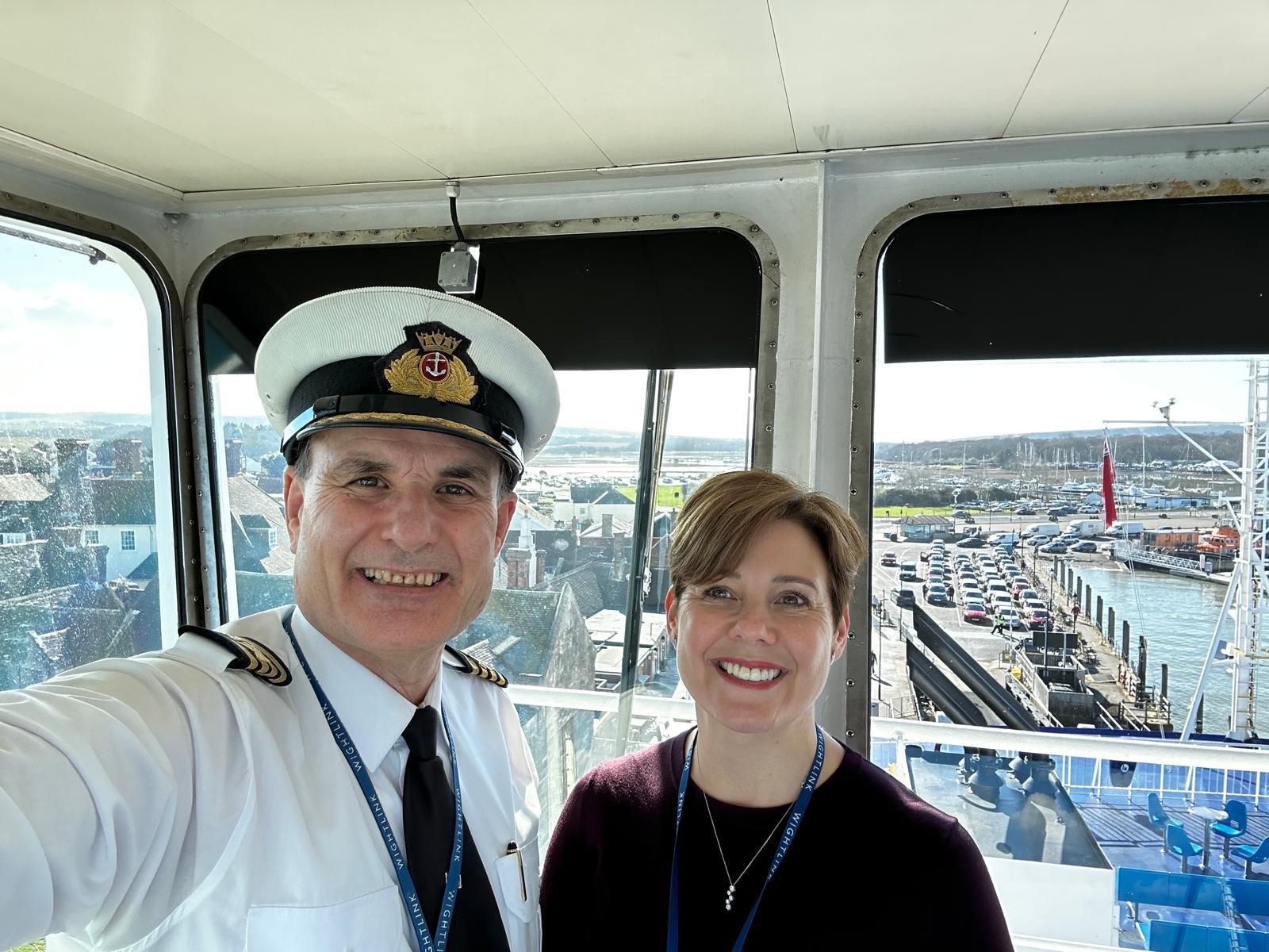 Wightlink Chief Executive Katy Taylor and a ferry captain on the bridge of a Wightlink vessel overlooking a ferry terminal and harbour.
