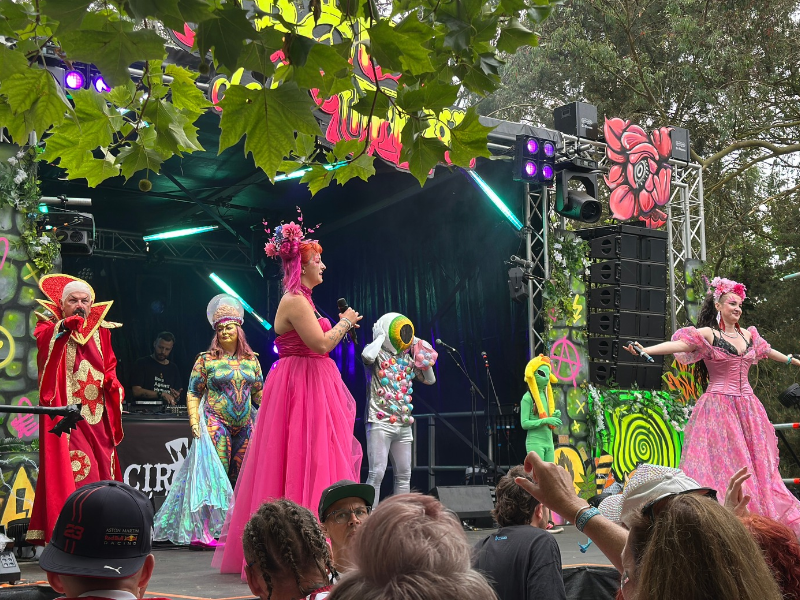 Costumed people perform on a stage under the trees at a festival