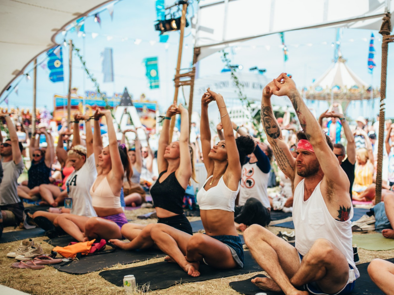 A group of people doing yoga, sitting on mats, in a tent at a Festival (courtesy Callum Baker)