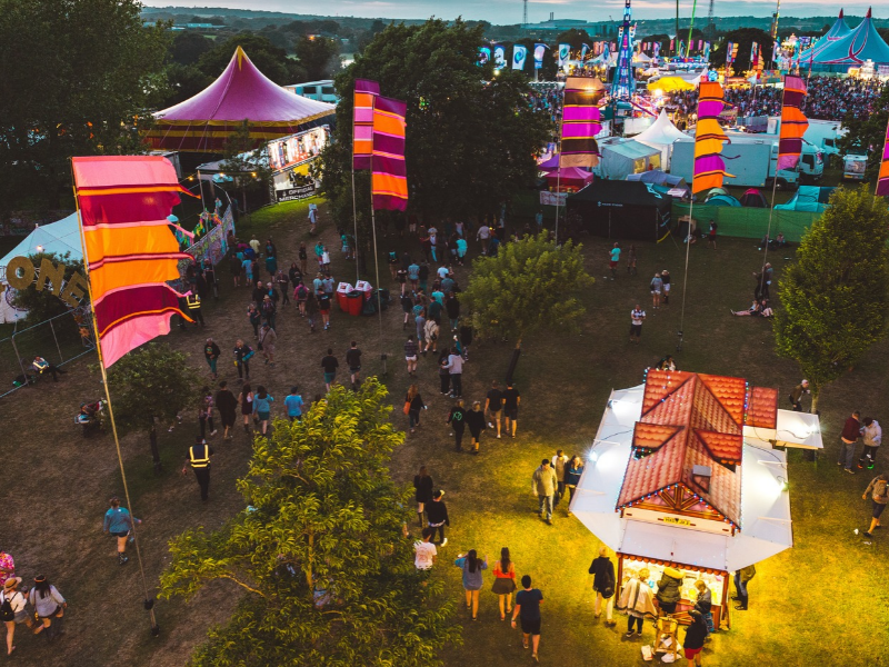 An aerial view of a festival at night showing people, food stalls, flags, tents and fields