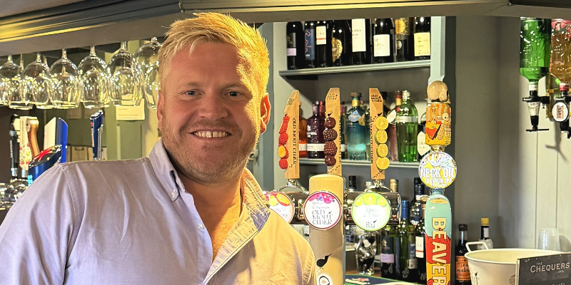 A man - head and shoulders - facing the camera and smiling. In the background is the bar of a pub.