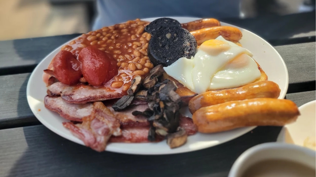 A full English breakfast, two fried eggs, four golden brown sausages, fried tomato, backed beans, black pudding, fried mushrooms and several rashers of bacon.