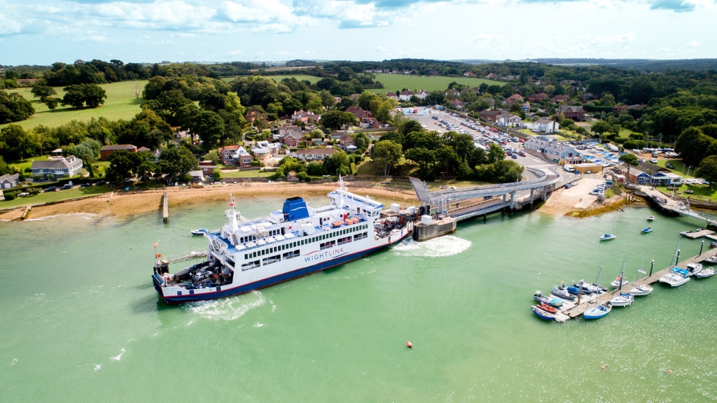 Aerial view of a Wightlink ferry arriving at Fishbourne terminal, with surrounding waterfront homes, marina berths and countryside.