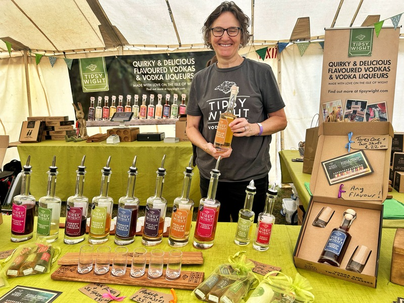 A woman standing behind a market stall full of liqueur bottles