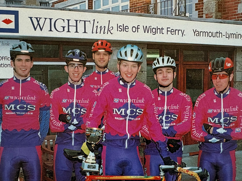An historic image of Wightlink MCS Cycle Race Team on their bikes and in branded kit, outside Wightlink's Yarmouth terminal