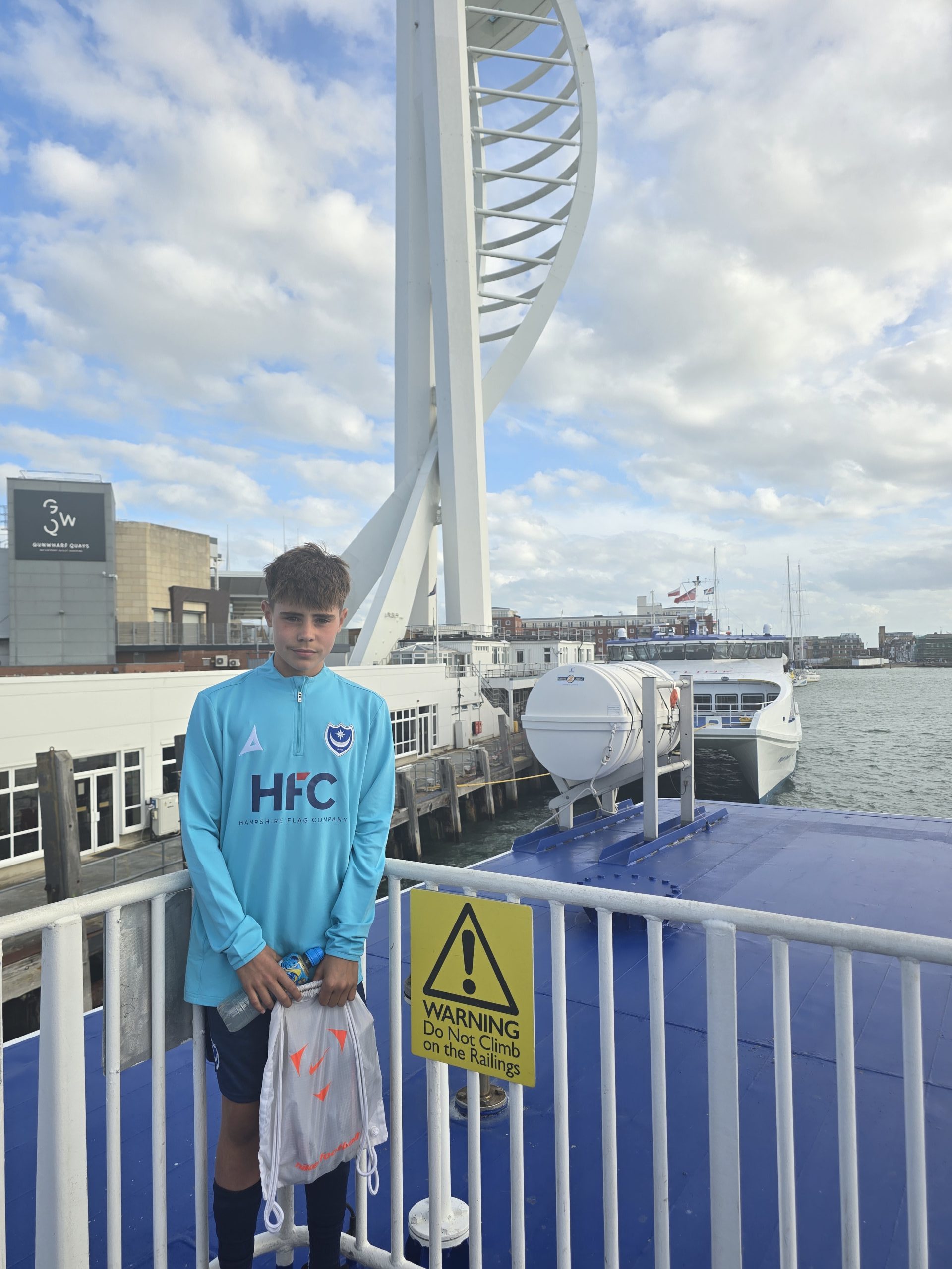 Young Portsmouth FC community programme player aboard a Wightlink ferry arriving in Portsmouth, with the Spinnaker Tower visible in the background.