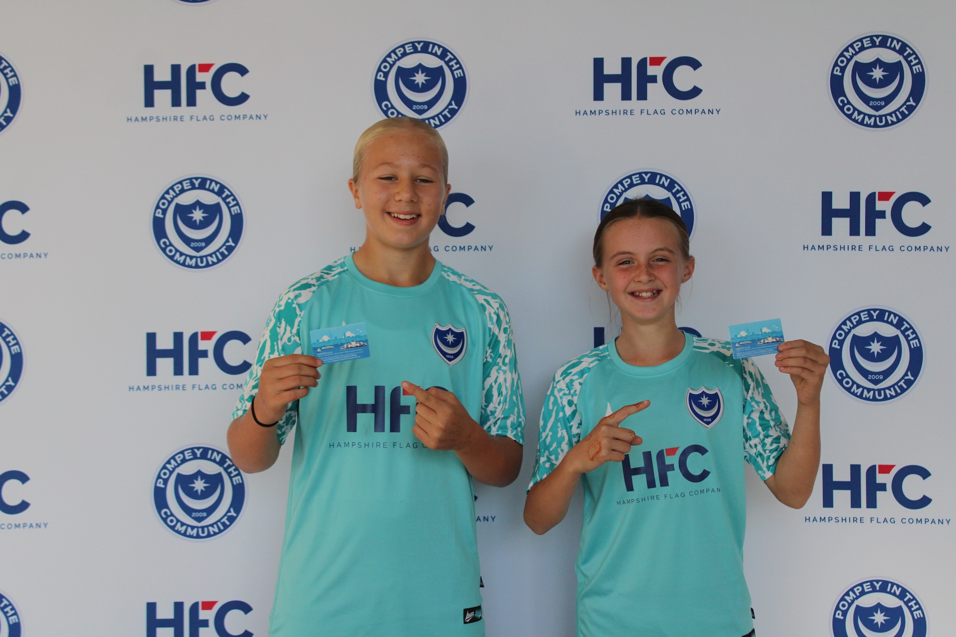 Two young Portsmouth FC community programme players holding Wightlink ferry travel passes provided to support access to training and matches.