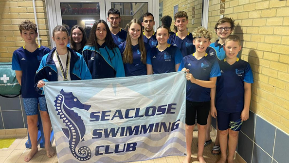 Members of Seaclose Swimming Club pose with the club banner at a swimming venue after a competition.