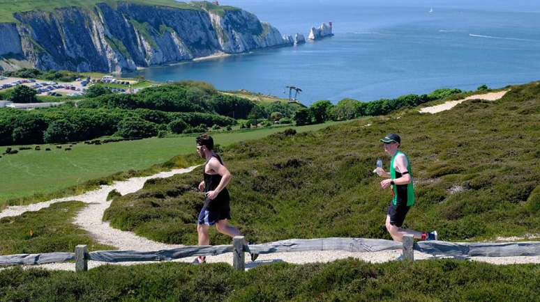 Runners running along a coastal path near the Needles, Isle of Wight