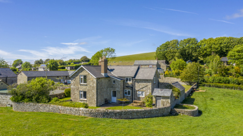 A traditional stone farm cottage set in green fields, with a circular wall around it